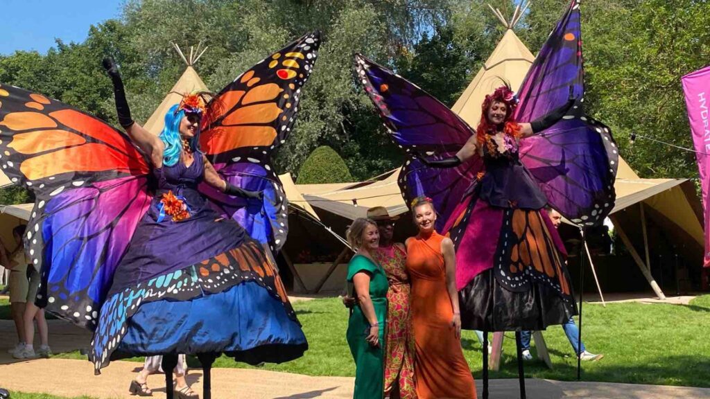 Butterfly stilt walkers posing with guests at a corporate conference festival outside in summer weather.