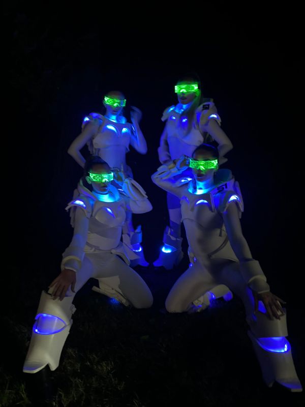 Sci fi glow girls in LED suits posing for camera at corporate festival event.