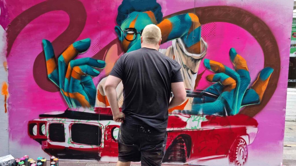 Artist standing in front of large graffiti mural.