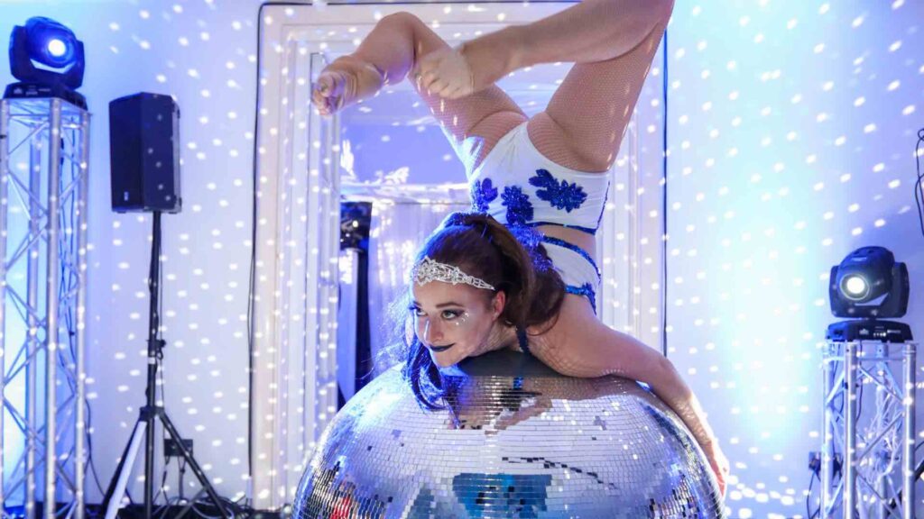 Contortionist on glitter ball performing acrobatics at Winter Wonderland theme.