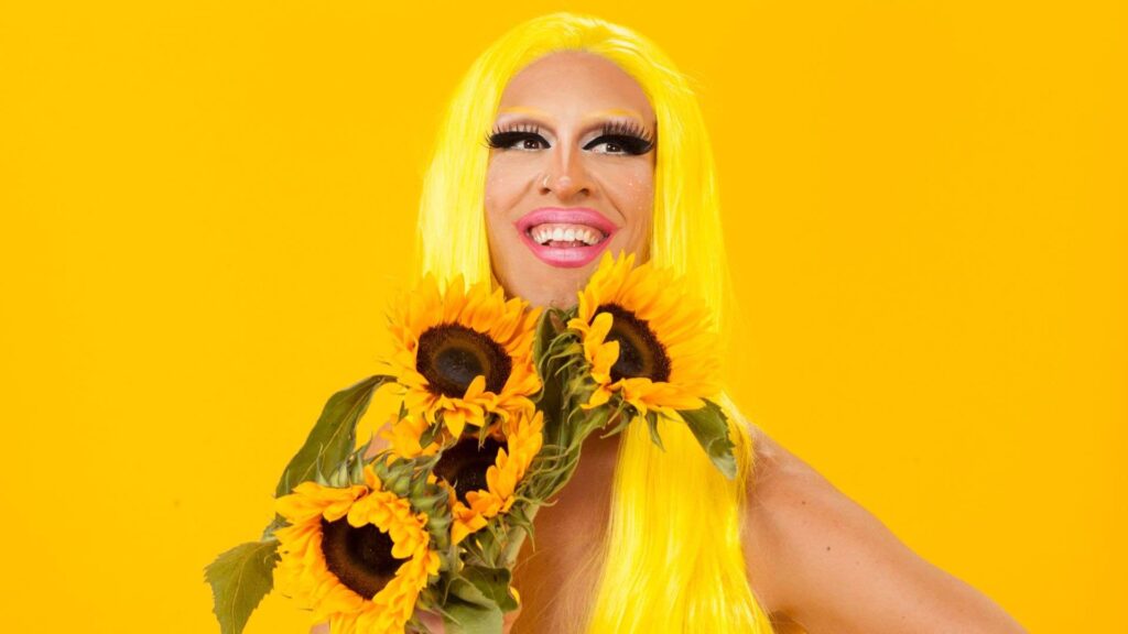 Charismatic drag queen posing with sunflowers against yellow background