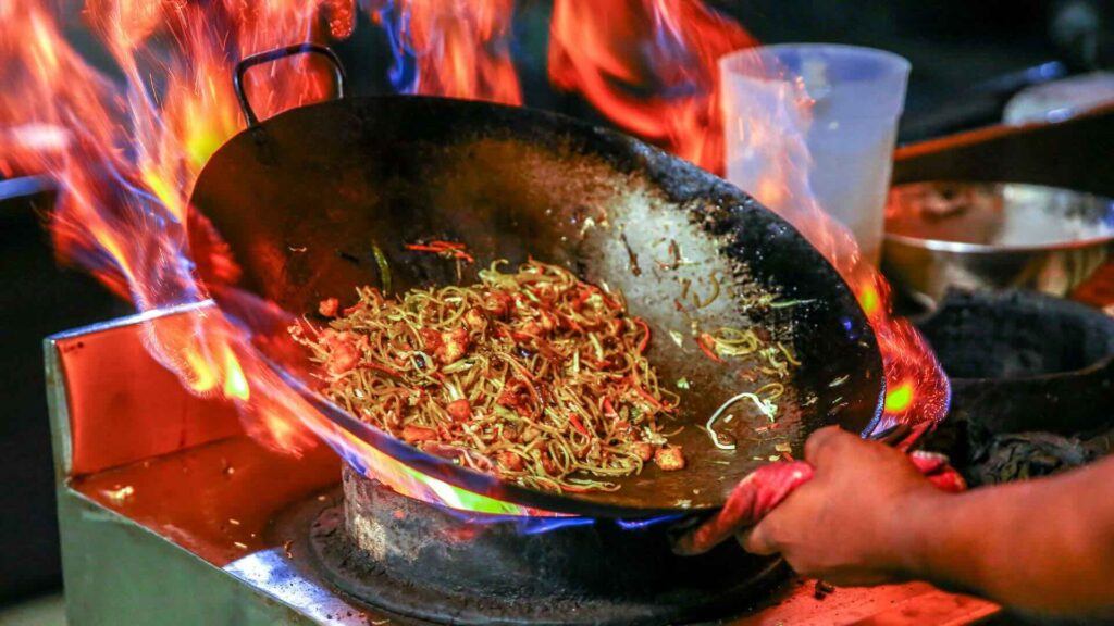 Large pan with noodle dish on a live flame.