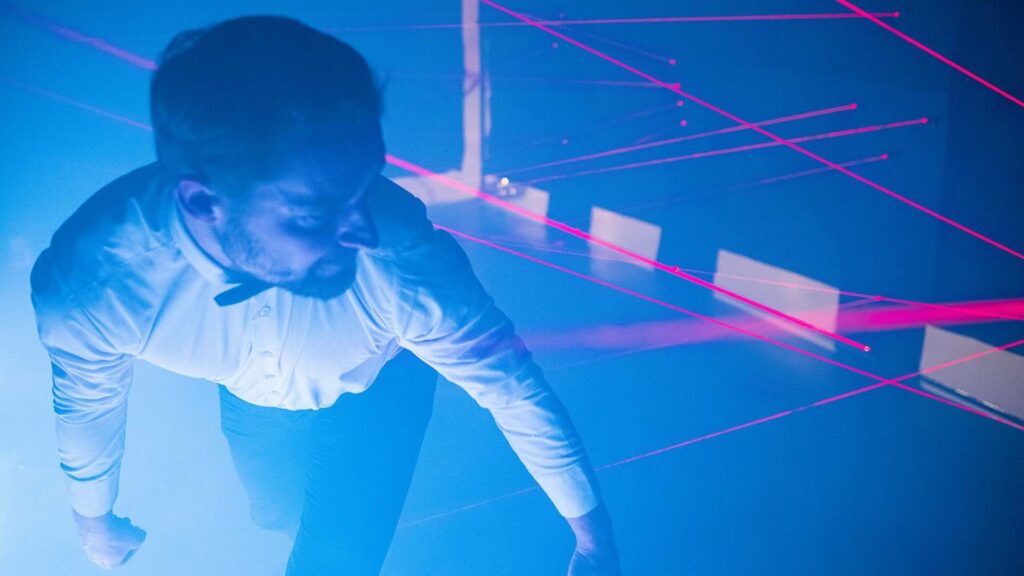 A man playing a laser maze game while dodging red laserbeams as conference team activities