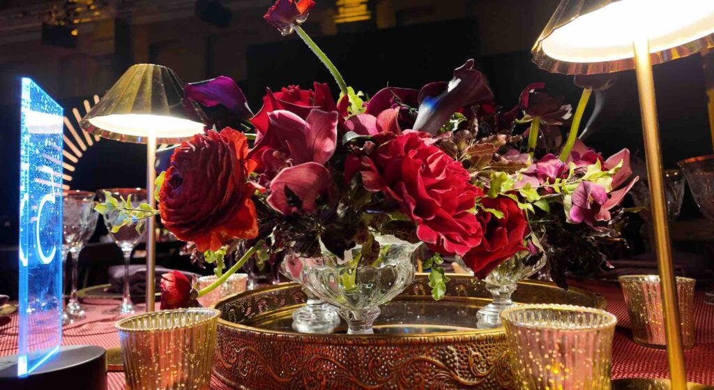Beautiful red flowers in ornate 1940s deco vases sat on a gala dinner table as part of the table centrepiece decor with gold and red finishes.