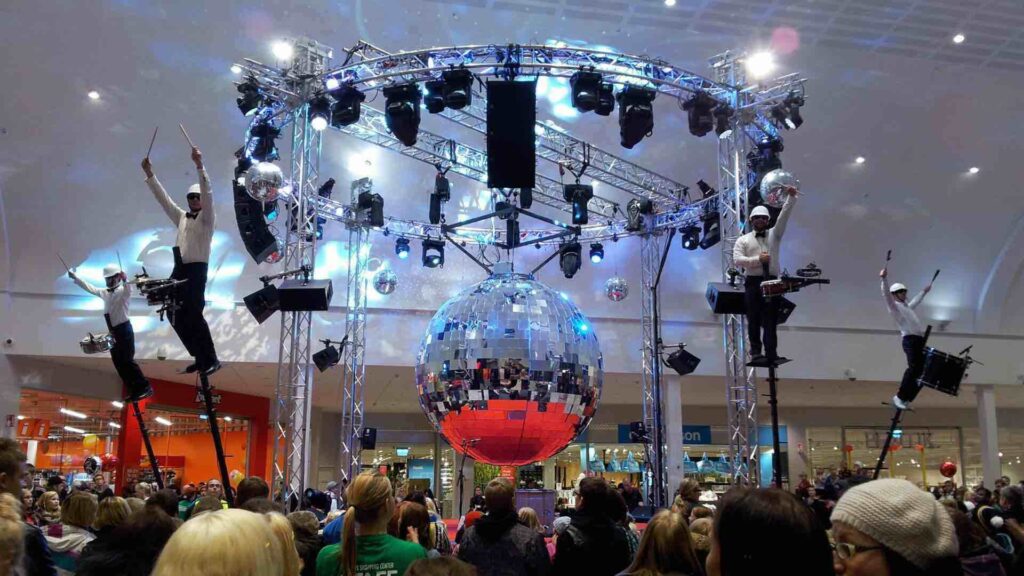 Sky drummers leaning over attendees as they entertain at an event with giant mirrorball