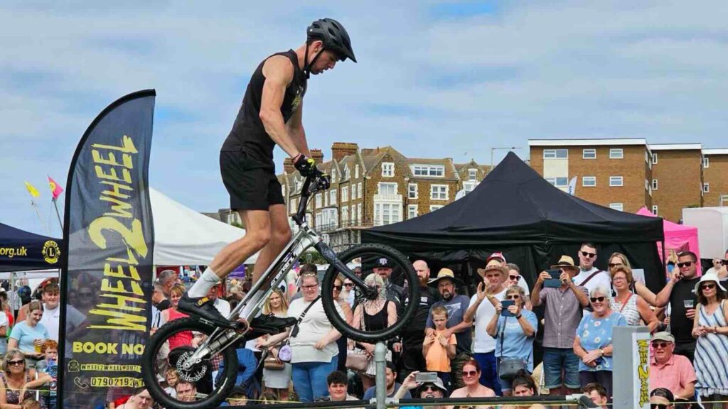 A mountain bike performer doing a wheelie in front of a large outdoor crowd