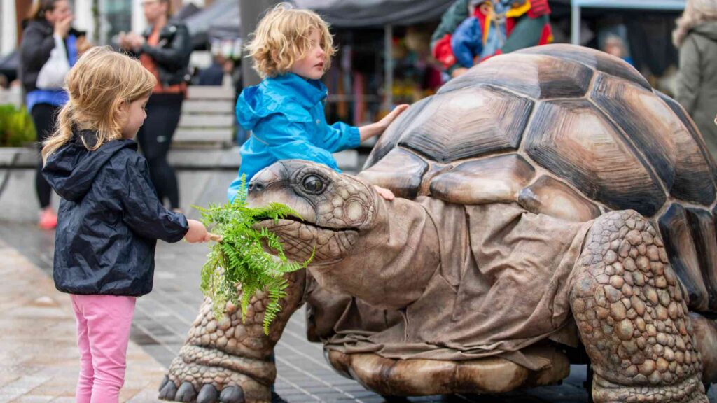 A young child interacting with a lifesize tortoise performer