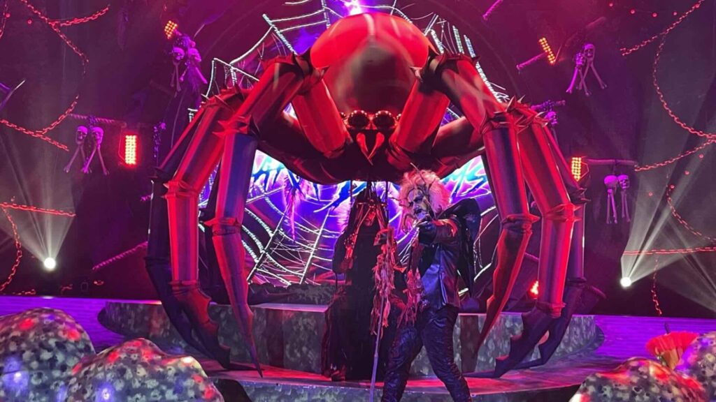 Giant bespoke large-scale spider puppet prop on stage behind halloween themed performers.
