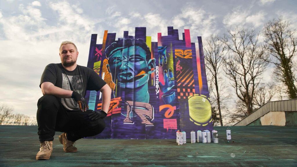 A mural artist posing in front of their mural