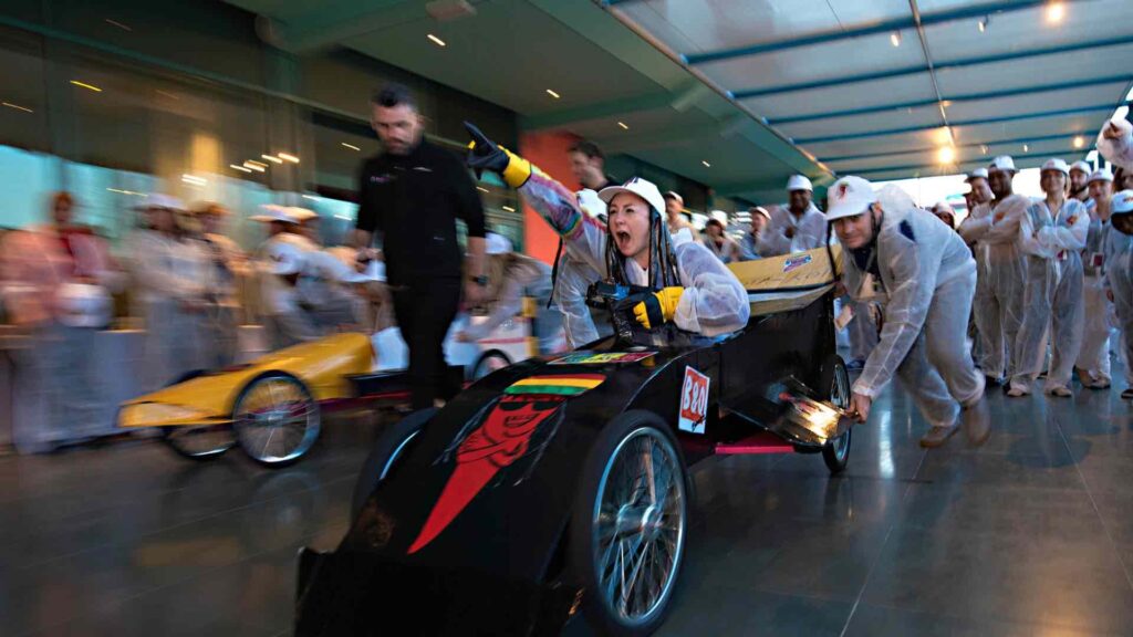 Formula one team building cart challenge showing a lady employee being pushed by other employees in their make shift cart for corporate fun day entertainment.