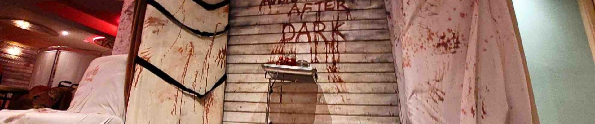 The "AVOID THE WARD AFTER DARK" set design features a gory medical tray, ominous table with straps, and a chilling electrolysis machine, setting a nightmarish tone.