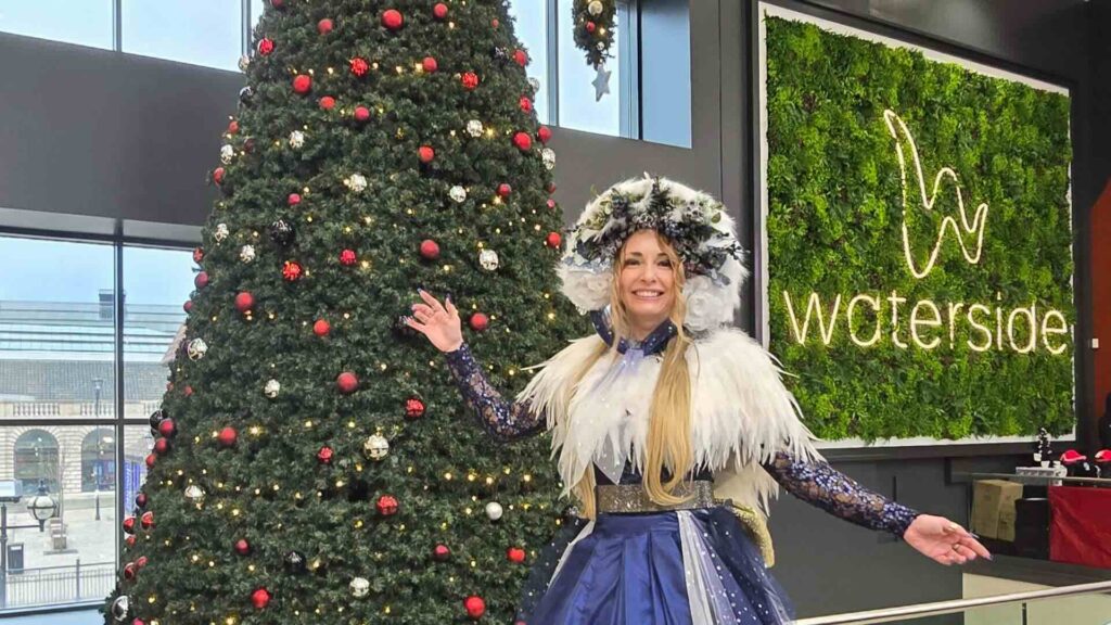 A Carol Singer Stilt Walker posing with a Christmas tree