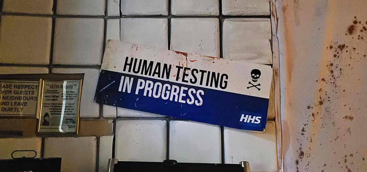 A chilling sign reading “Human Testing in Progress” adds an unsettling edge to the Asylum-themed Halloween decor.