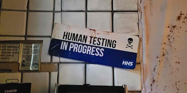 A chilling sign reading “Human Testing in Progress” adds an unsettling edge to the Asylum-themed Halloween decor.