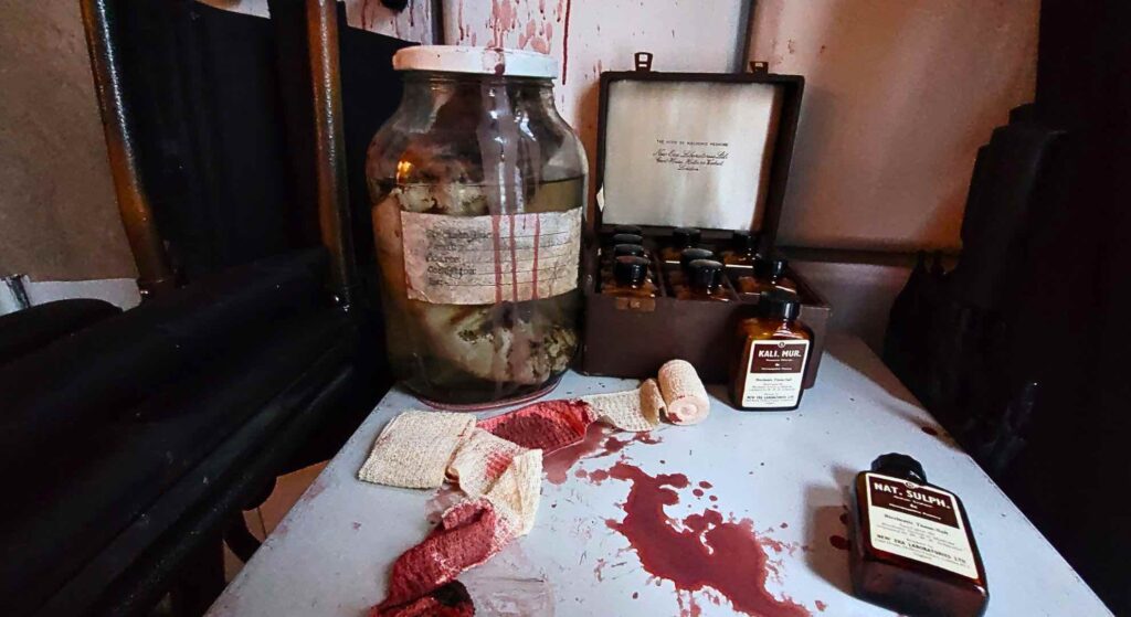 Medicine boxes and jars, accompanied by bloody rags, sit atop a filing cabinet, completing the chilling atmosphere of the Asylum-themed event.