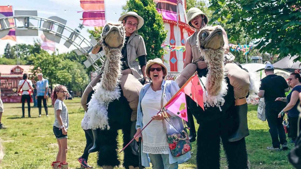 Two walkabout ostrich performers at an outdoor event with a crowd of guests