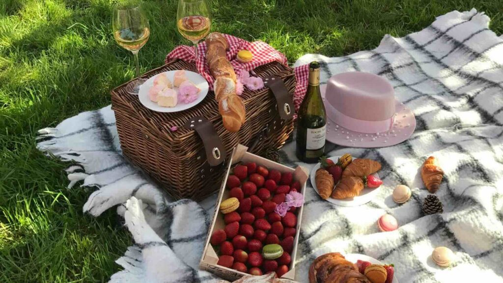 Picnic basket on blanket filled with strawberries and sweet treats.