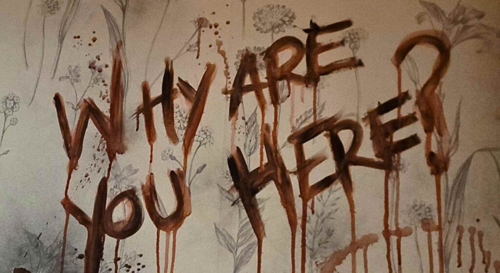 A blood-scrawled messageโโWHY ARE YOU HEREโโhaunts the wall of a nightmarish Asylum-themed Halloween scene.