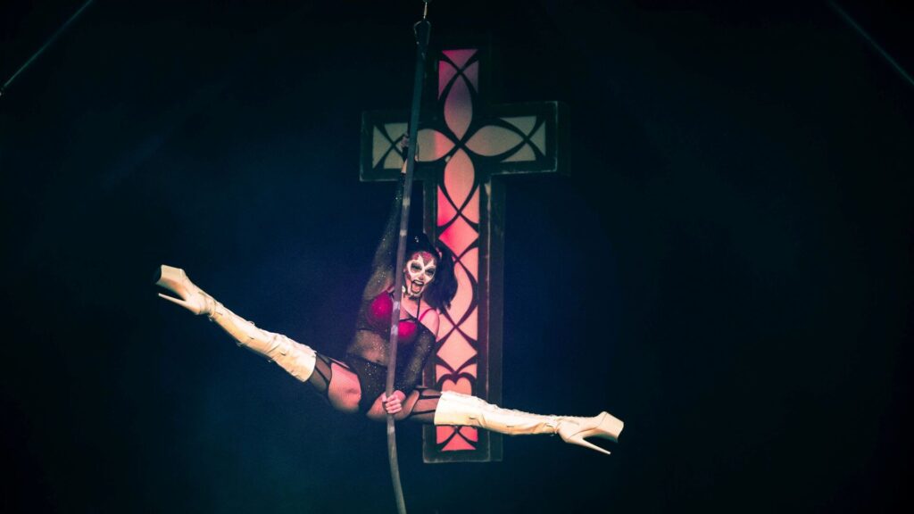 A Halloween themed aerialist in the air with a cross on the wall behind them.