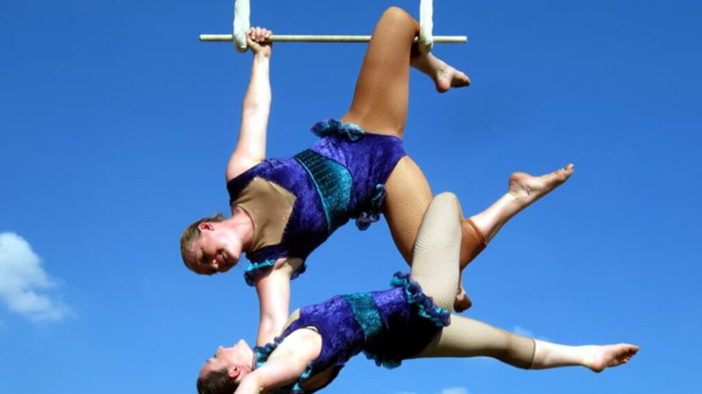 Two trapeze artists hanging from above at an outdoor event.