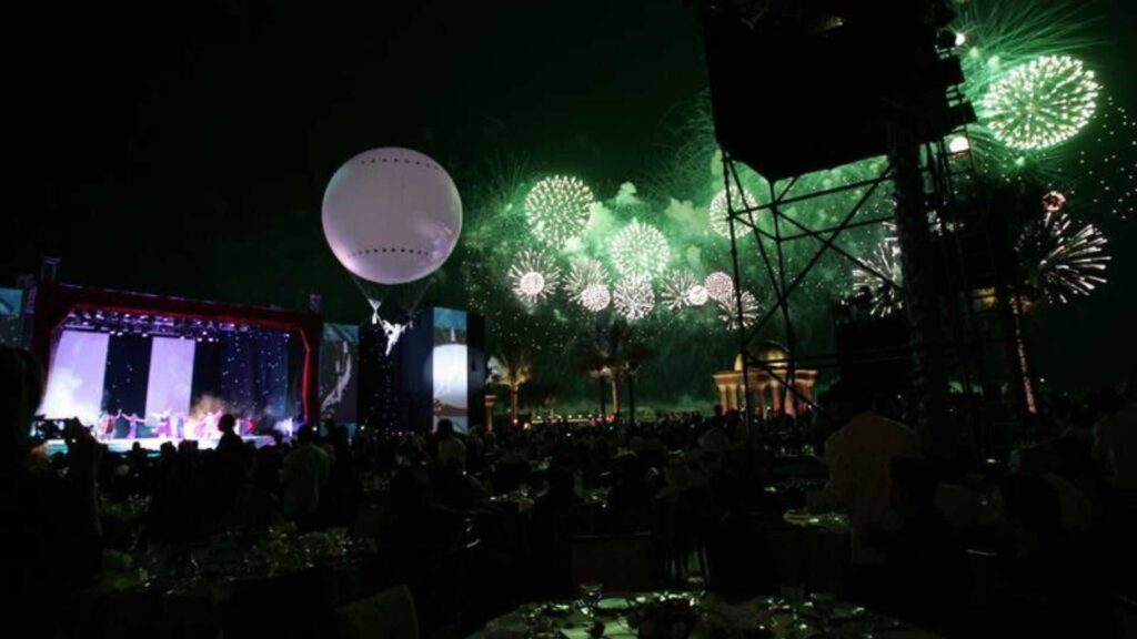 A balloon aerialist hanging above the crowd with fireworks.