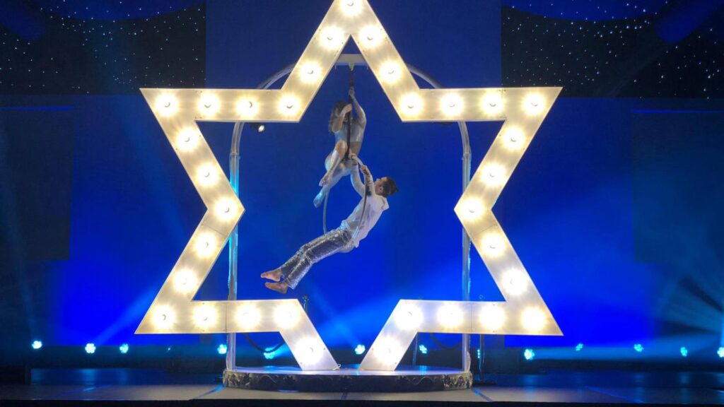 Aerial star acrobats handing from LED star prop that glows at a Christmas event.