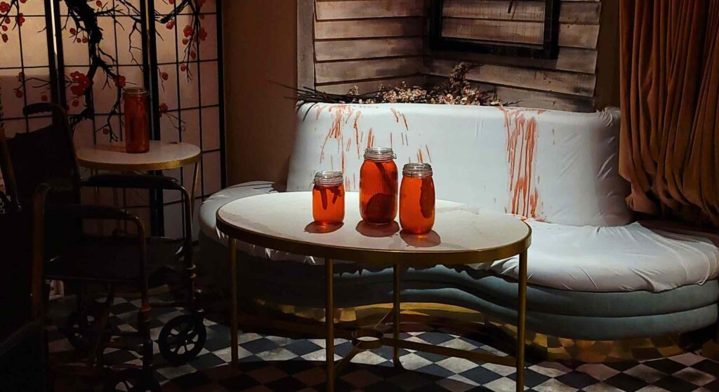 Three mason jars filled with unsettling contents rest on a table, with the interior of TABU nightclub looming in the background, adding a disturbing touch to the Asylum-themed event.