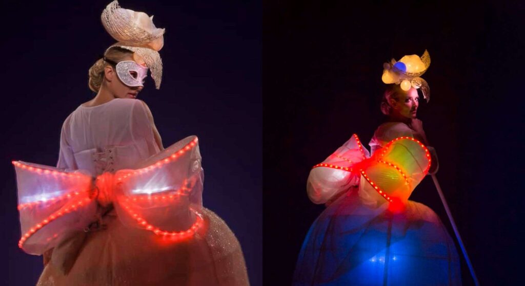 Stunning light up LED bow stilt walkers with elegant costumes posing with dark background.