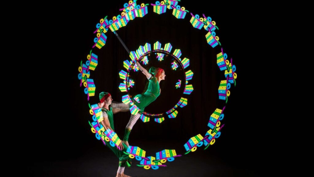 Christmas elf acrobats performing LED circus moves projecting Christmas presents.