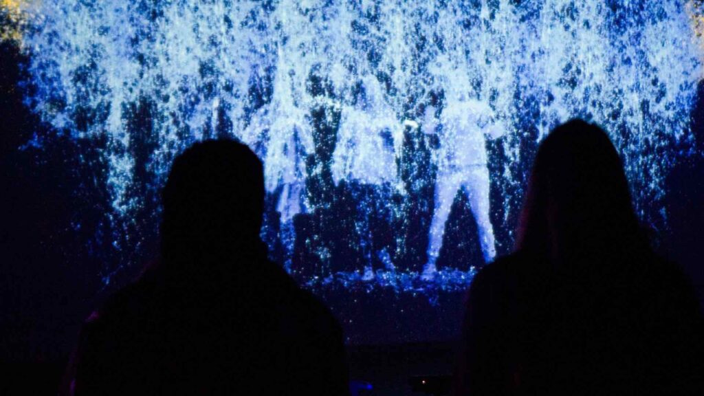 Two people's shadows as they stand in front of an LED wall.