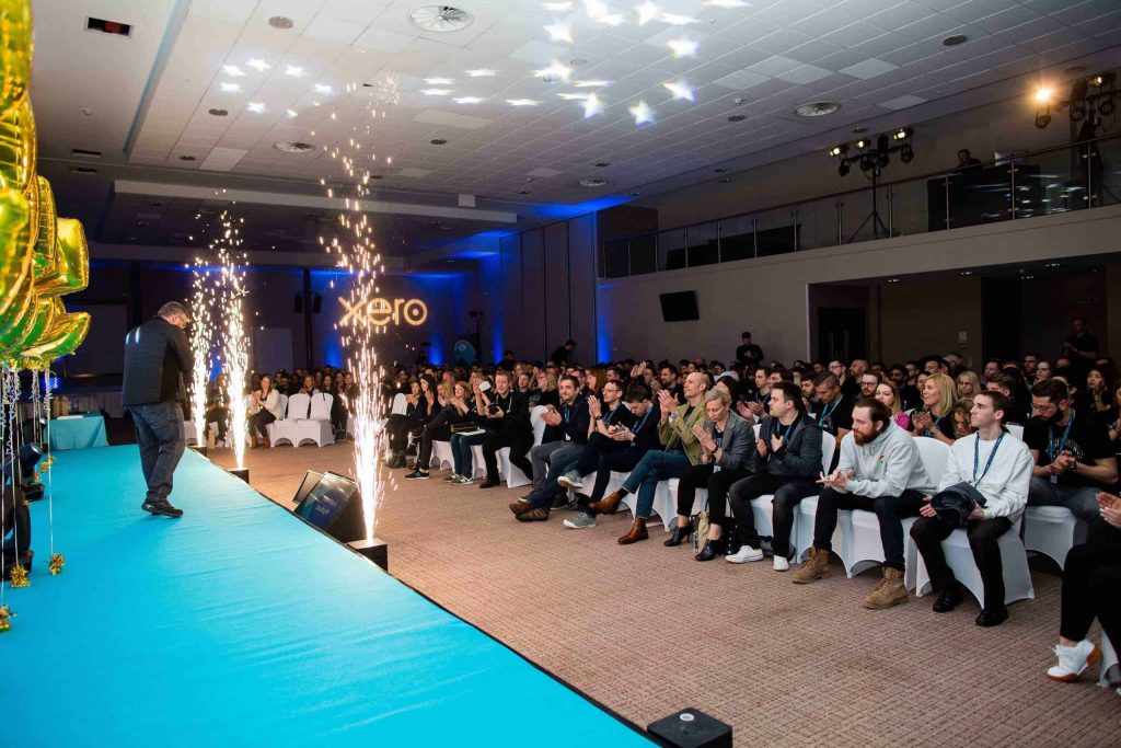 A man on stage presenting at a Xero conference with pyro.