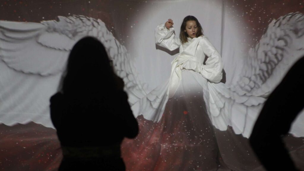 Lady with angel wings performing on stage being filmed at a luxury product launch event.