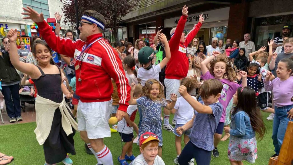 PE teachers walkabout act amusing crowds of children at family fun day event.