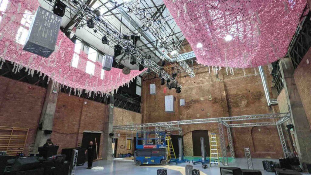 An event in Shoreditch being set up, with rigging and lighting next to pink leafy decor.