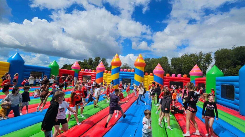 Worlds biggest bouncy castle in vibrant colour's on a sunny day with children bouncing on it.