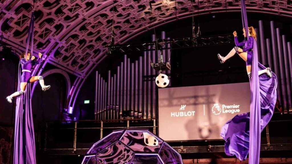 Two football themed aerial silk performers hang in the air at an event, putting on a choreographed routine together.