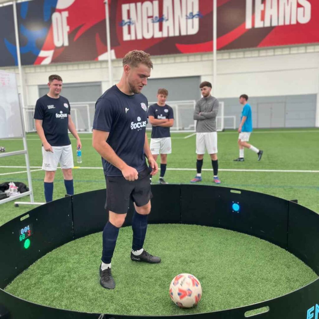 A fast feet football game at an event, with a man stood inside the circle hitting the ball at LED light targets.