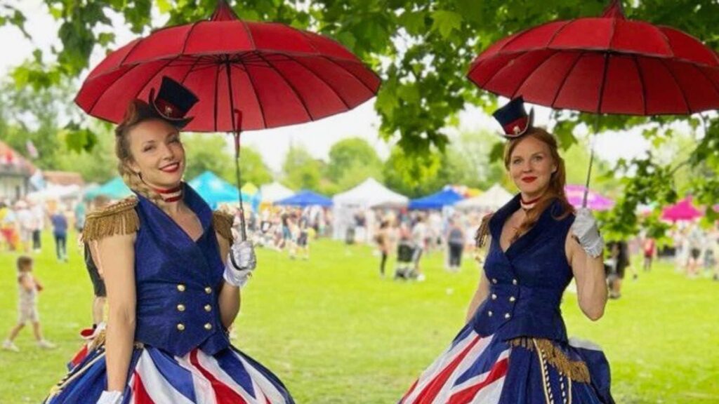 Two ladies wearing Union Jack dresses at a large outdoor event with a big crowd behind them.