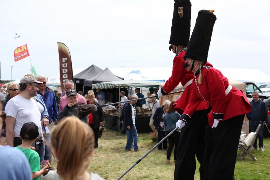 Two stilt walking royal guards interacting with guests at a large outdoor festival event.