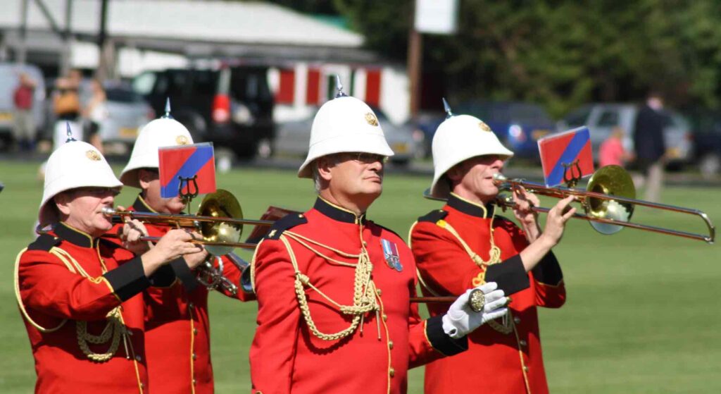 A traditional military band performing for a British event in their red attire with trumpets.