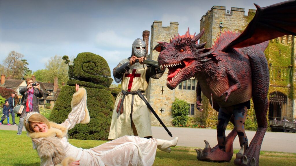 A St. George's Day dragon looming over a performer on the ground fiercely, with a person in the background taking photos.