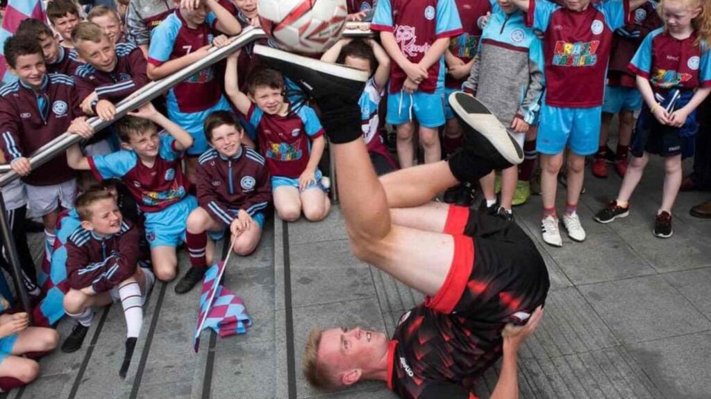 Football freestyler performing tricks during walkabout entertainment at outdoor event.
