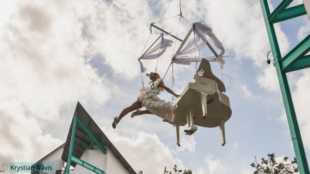Ethereal live piano aerial act performing in the sky at UEL London with floating ribbons and white piano.