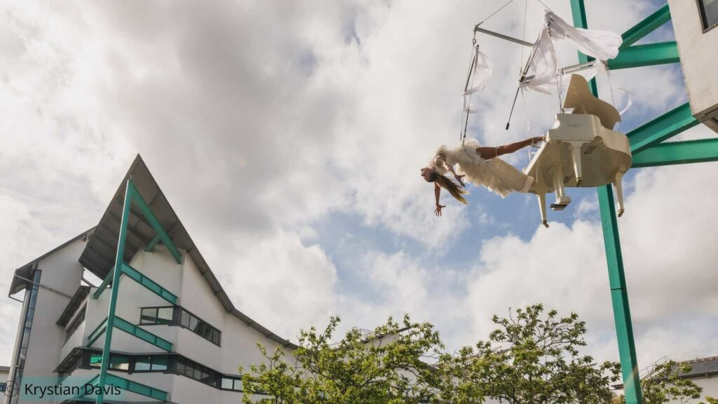 A daring aerial act performing tricks from a hoisted piano as part of an immersive signature bespoke show by JCEM.