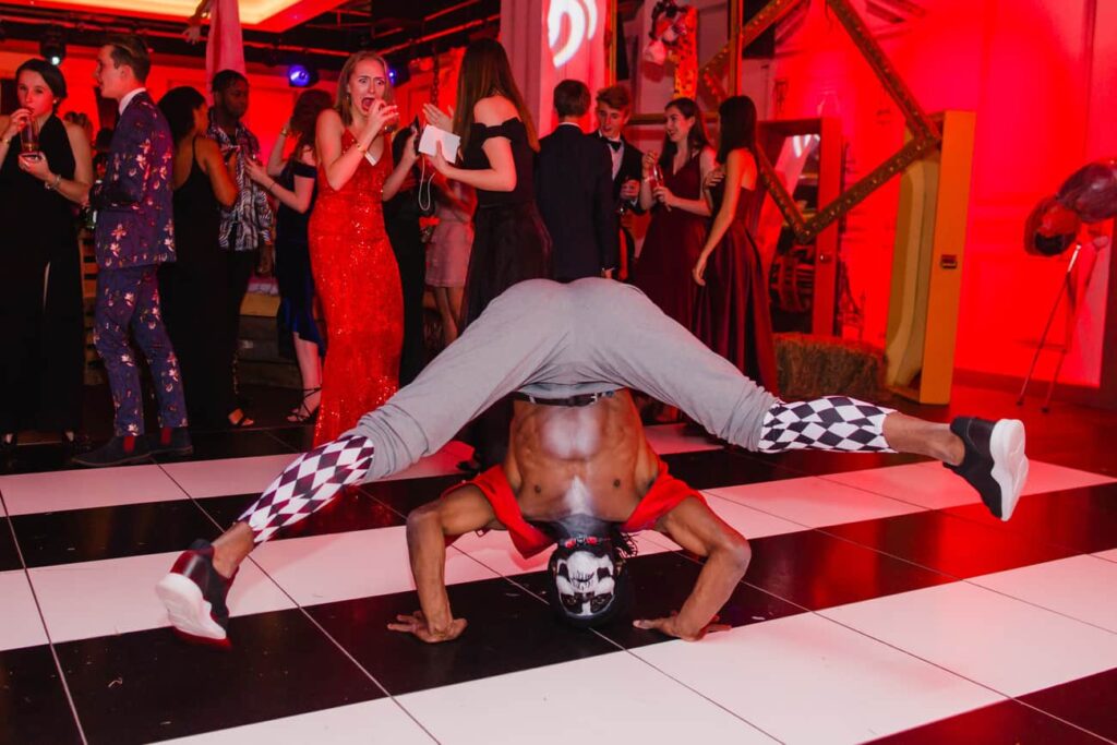 A Halloween performer dancing on the stage as people looking at him in the background.