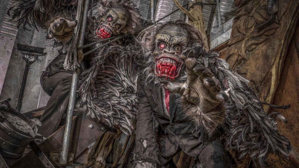 Two feral ape creature performers with bloodied mouths crawling towards the camera.