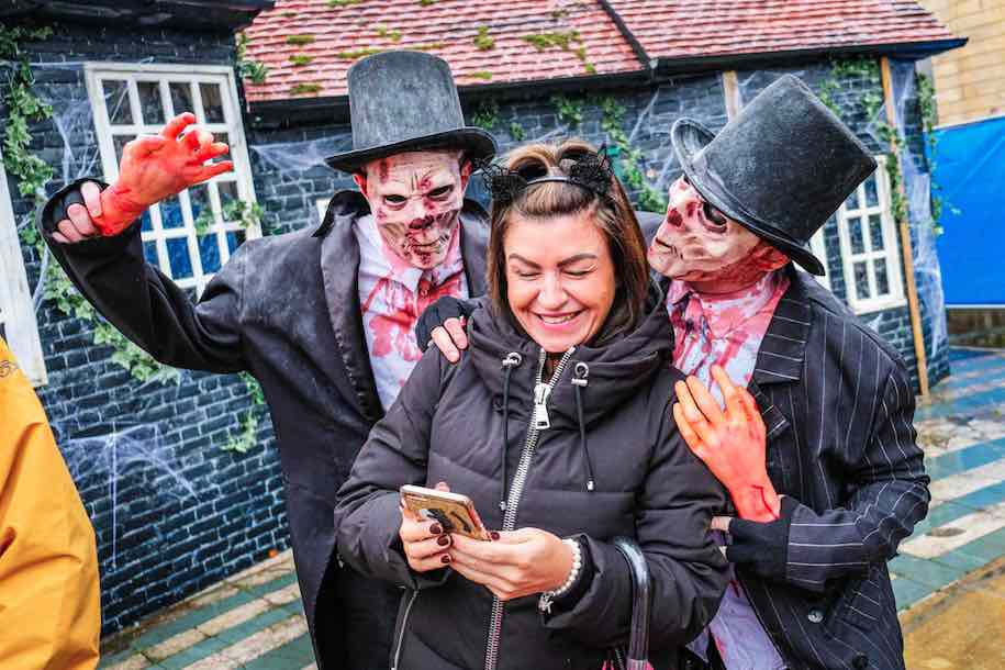 Two zombie walkabout performers posing with a laughing guest at Southport Trick or Treat Street Halloween event.