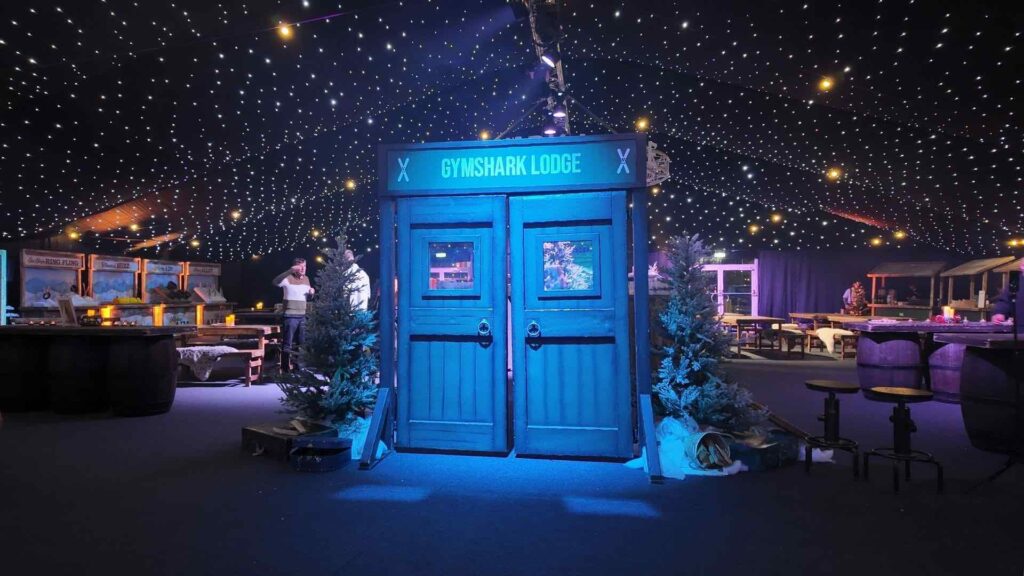 Freestanding blue alpine lodge doorway with GYMSHARK LODGE sign at a corporate Christmas party