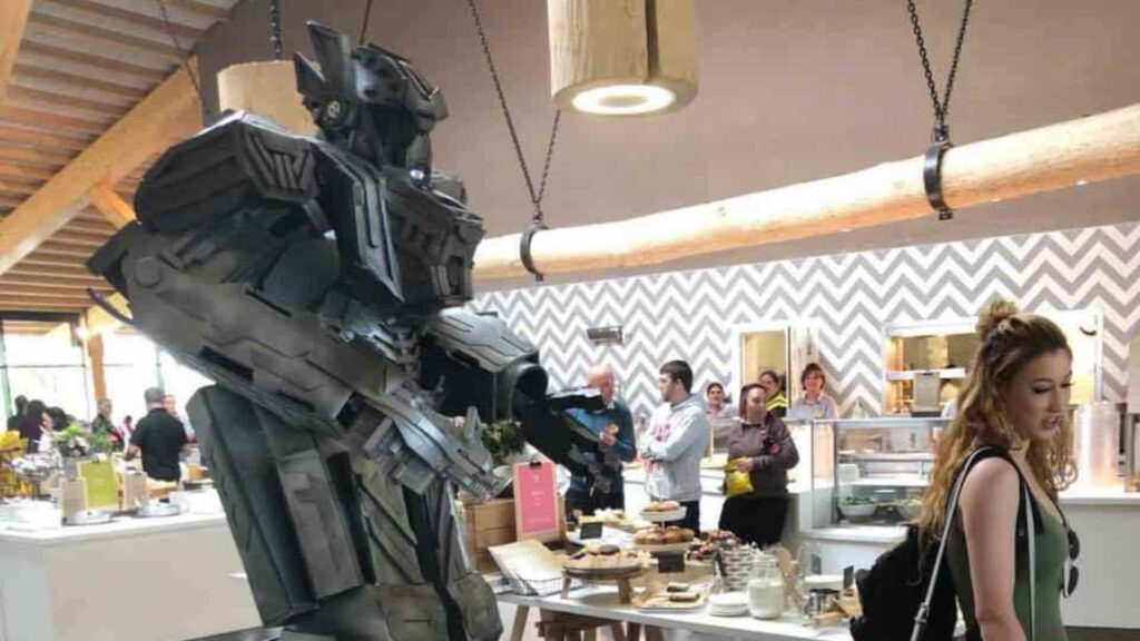 Ten foot tall vocal robot performer towering over guests beside a catering counter at an indoor event