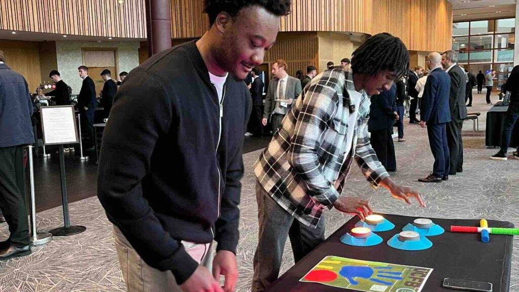 Two delegates playing a branded light reaction game at a corporate event while other guests network in the background